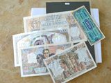 quatre billets de banque différents posés sur une table, à côté d'un passeport