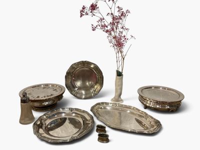 a vase with a flower in it next to a bunch of silver plates