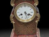 une horloge rouge et dorée posée sur un socle, sur fond noir
