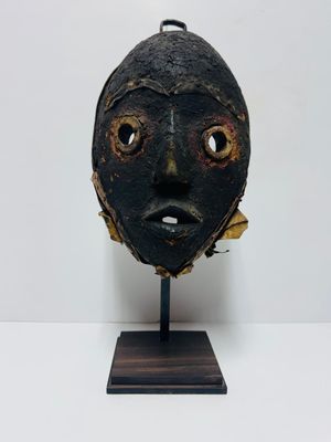 a black mask on a wooden stand on a white surface