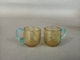 pair of yellow glass cups with blue handles sitting on a white surface