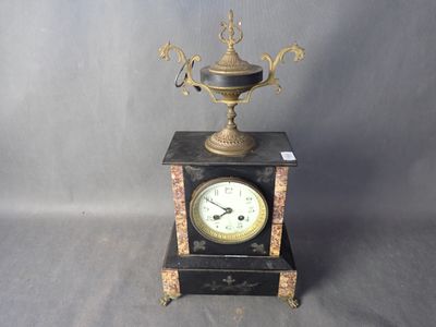 une horloge noire et dorée surmontée d'une coupe dorée