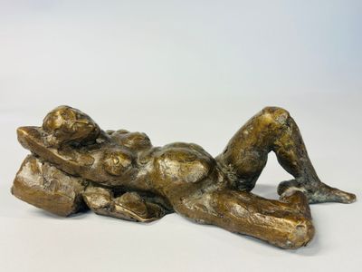 bronze statue of a woman laying on her stomach on a white surface