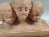 sculpture of three heads of a woman and three children on a wooden base