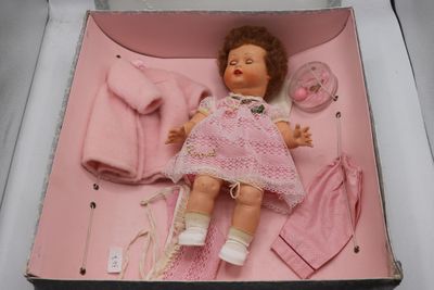 une poupée dans une boîte rose, avec des vêtements et une tétine