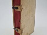 an old book with a red cover sitting on a white surface