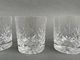 three crystal tumblers are lined up on a gray surface