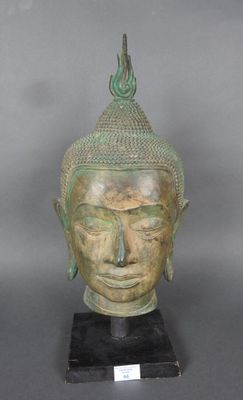 statue représentant une tête de Bouddha sur un socle noir, avec un fond gris