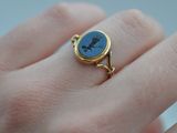 a woman ' s hand holding a gold ring with a blue stone on it