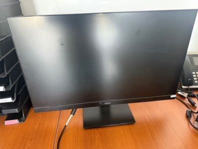 un écran d'ordinateur posé sur un bureau, devant un téléphone
