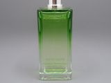 une image représentant un flacon de parfum vert posé sur une surface grise