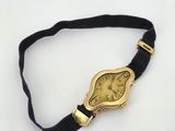 a gold wrist watch with a black band on a white surface