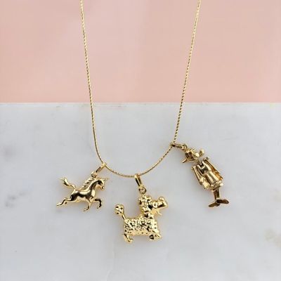 un collier plaqué or orné de quatre breloques, posé sur une surface en marbre