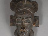 an old wooden mask hanging on a wall on a gray background