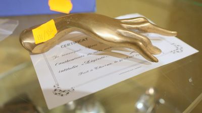 une statue en or représentant une main tenant un bout de papier sur une table en verre