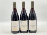 trois bouteilles de vin rouge sont posées sur une surface blanche