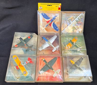 Plusieurs petits avions en plastique sont exposés dans une vitrine posée sur une surface noire.
