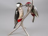 figurine d'oiseau plaquée argent, aux plumes rouges et noires, posée sur une branche