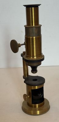 Un vieux microscope est posé sur une table en bois.