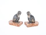paire de figurines noires et argentées représentant un oiseau, posées sur un socle en pierre