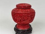 a red vase sitting on a stand with a bird on it