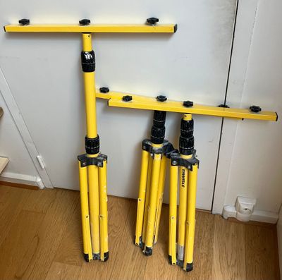 Deux trépieds jaunes sont posés sur un plancher en bois, près d'un mur.