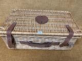 un panier de pique-nique en osier avec des anses en cuir, sur fond marron