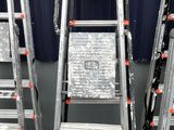 Plusieurs échelles métalliques sont empilées contre un mur bleu.