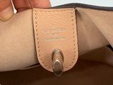 someone is holding a tan purse with a black handle and a silver ring