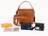 un sac en papier brun, un appareil photo et quelques autres objets posés sur une surface blanche