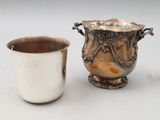 a silver cup next to a silver vase on a table