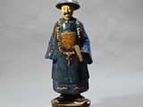 une statue en bois représentant un homme coiffé d'un chapeau et tenant un livre