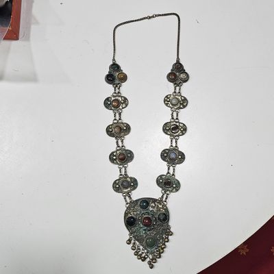 silver necklace with multi colored stones on it on a white table