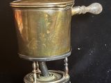 cafetière en laiton plaqué sur son support, sur fond noir