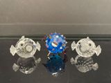 trois figurines de poissons en verre posées sur une table en verre