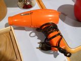 un sèche-cheveux orange posé sur une table, à côté d'un vase rouge