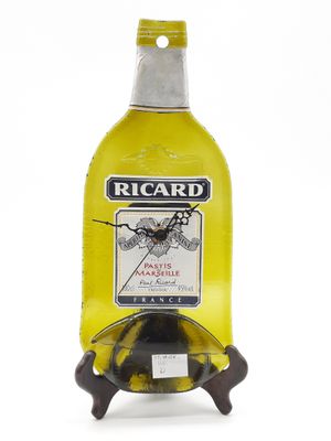 une bouteille jaune de vin Ricard posée sur un socle, sur fond blanc