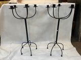 une paire de chandeliers en fer noir avec des bougies posées sur des socles, le tout sur une nappe blanche