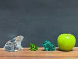 a green apple sitting next to three pieces of glass