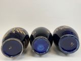 three blue vases with gold designs are lined up on a white surface