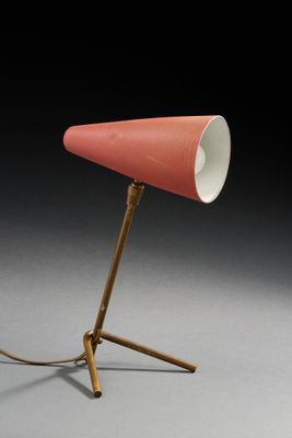 une lampe orange posée sur un trépied, devant un fond noir