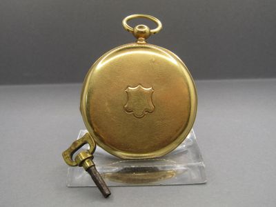 a gold pocket watch with a key on a stand