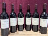 six bottles of red wine are lined up on a wooden table