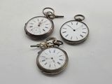 three silver pocket watches with roman numerals on them on a white surface