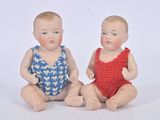 two baby dolls sitting next to each other on a white surface
