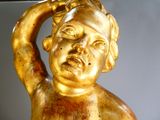 a gold statue of a child holding a bird on his head