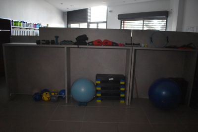 un box de bureau faiblement éclairé, équipé d'appareils de musculation et d'une balle bleue