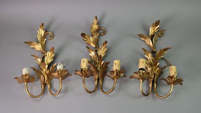 three gold leaf wall sconces mounted on a white wall