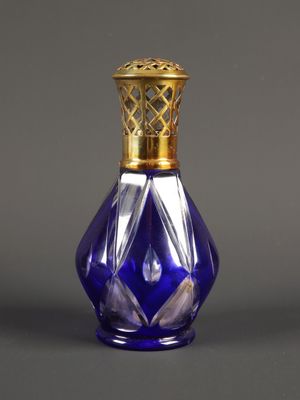 flacon de parfum en verre violet avec un bouchon doré, posé sur une surface grise