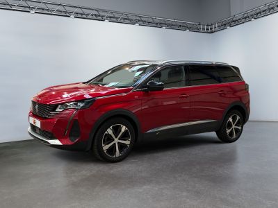 La voiture rouge est garée dans une grande pièce aux murs blancs.